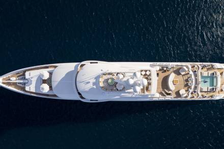 A luxurious white yacht with multiple decks and a pool sails on the deep blue ocean.