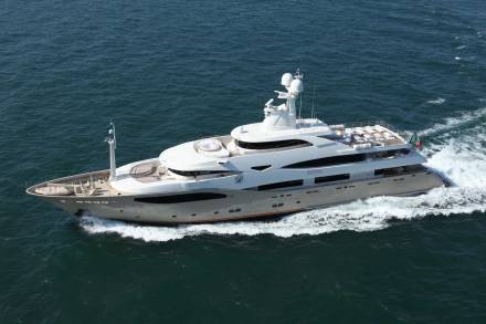A large white yacht cruises through calm blue water, leaving a foamy wake behind it.