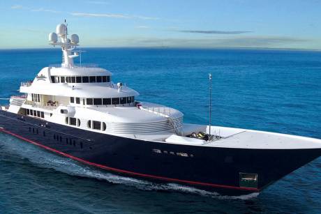 A luxurious superyacht glides through the deep blue ocean under a clear sky.