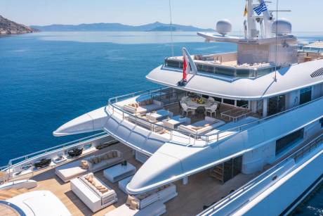 Luxurious white yachts with ample deck space for lounging and dining are anchored in the clear blue waters of a Mediterranean bay.