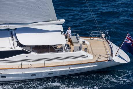 A man steers a luxurious yacht through the deep blue ocean under a bright sky.