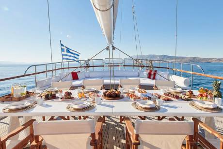 A beautifully set table awaits on the deck of a yacht, offering a delightful spread of breakfast treats against a backdrop of the sparkling blue sea.