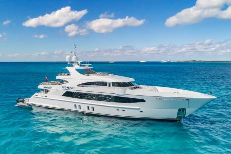 A luxurious white yacht named "BIG SKY" glides through the crystal-clear turquoise waters under a bright blue sky dotted with fluffy clouds.