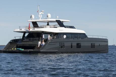 A sleek, modern yacht named "MANTA" cruises on calm blue waters under a clear sky.