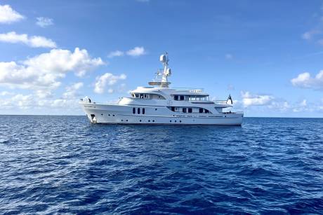 A sleek white yacht glides across the deep blue ocean under a bright sky dotted with fluffy clouds.