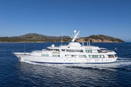 The majestic yacht Lady Beatrice glides through the deep blue waters under a clear sky, with rugged, tree-covered islands in the background.
