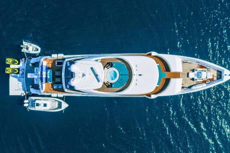 An aerial view captures a luxurious yacht at sea, complete with jet skis and a tender boat.