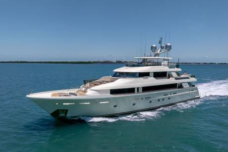 A luxurious white yacht cruises through clear blue waters under a bright sky.