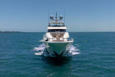 A sleek white yacht cruises through the turquoise ocean under a clear blue sky.
