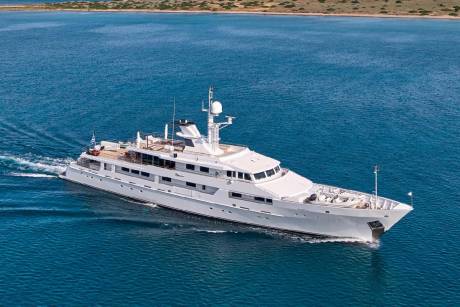 A luxurious white yacht glides through the serene blue waters near a sun-drenched coastline.