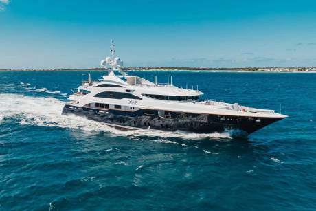 A luxurious yacht cruises through the azure waters off a tropical coastline under a clear blue sky.