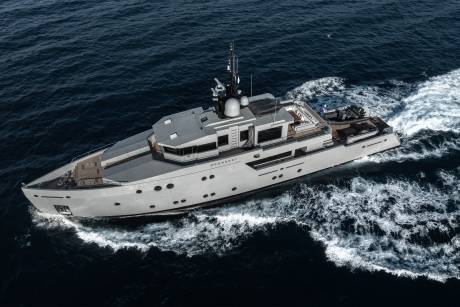 A large, gray yacht sailing across the deep blue ocean, leaving a trail of white waves in its wake.
