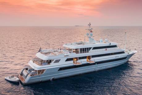 A large, luxurious yacht sailing across a calm, pink-hued ocean at sunset, with a serene horizon in the background.