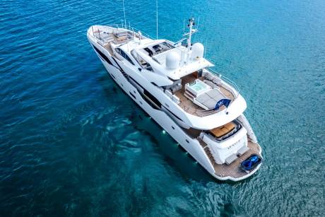 A luxurious white yacht with a jacuzzi on its upper deck floats on the clear blue ocean.