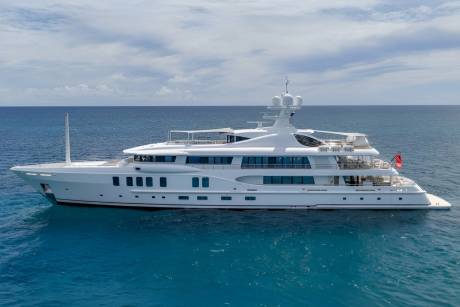 A large white yacht floats on calm blue water with a cloudy sky in the background.
