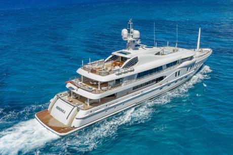 A large white yacht cruises through clear blue ocean water, leaving a white wake behind it.