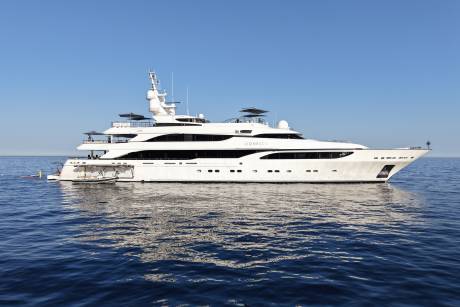 A large white yacht with multiple decks floats on calm blue water under a clear sky.