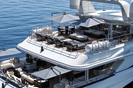 Luxurious lounge areas with umbrellas and seating are visible on the decks of a white yacht, set against a calm blue ocean.