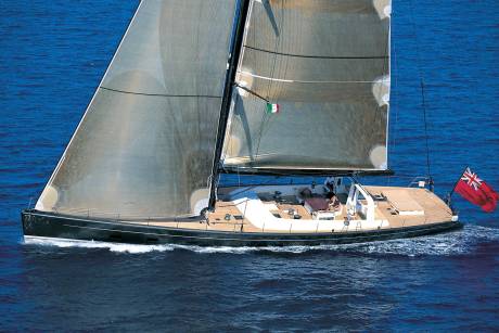 A sleek, dark sailboat with full sails glides across a deep blue ocean, its wake trailing behind it.