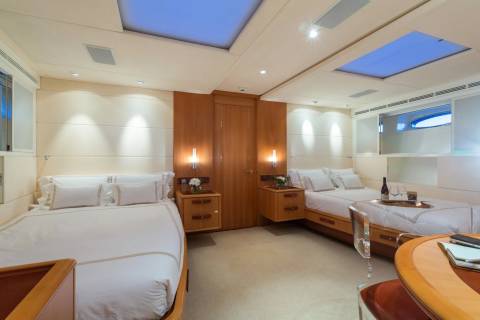 Luxurious twin beds are neatly made in this serene cabin, bathed in soft light from above.