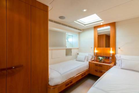 Luxurious twin beds with crisp white linens are nestled within a wood-paneled cabin, illuminated by a skylight.