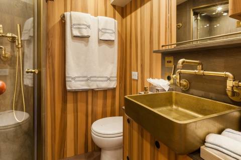 A luxurious bathroom features a brass sink and faucet, a toilet, and a shower with vintage-style plumbing.