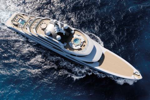 A sleek white superyacht glides through the deep blue ocean, leaving a trail of white foam.