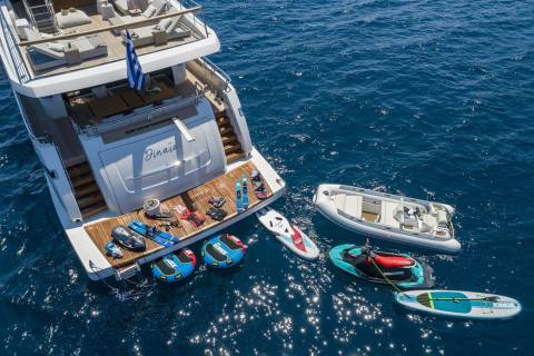 A luxury yacht is fully equipped with water toys, including jet skis, paddleboards, and inflatable tubes, ready for aquatic adventures.