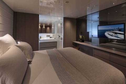Luxurious yacht interiors feature a serene bedroom with a sleek en-suite bathroom and a large television displaying a scenic ocean view.