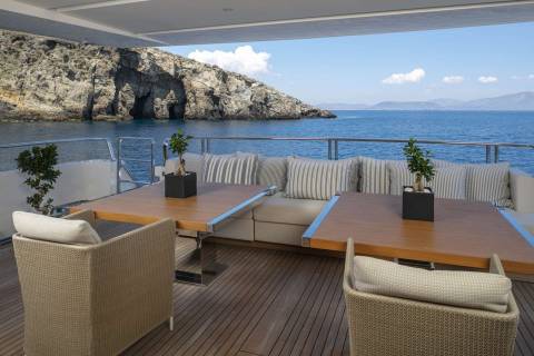 Dine al fresco on this luxurious yacht deck with stunning views of a rocky coastline and the azure sea.