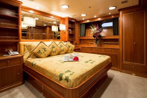 Luxurious yacht cabin features a plush bed adorned with floral linens and a tray of tea.