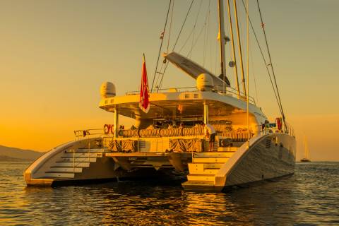 A luxurious catamaran glides through golden waters at sunset, its sleek design illuminated by the warm evening light.