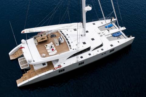 A majestic white catamaran yacht glides through deep blue waters under a clear sky.