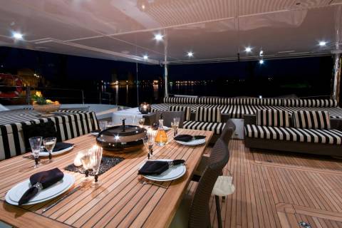 An elegant outdoor dining setup on a yacht deck is illuminated by soft lights against a dark night sky.