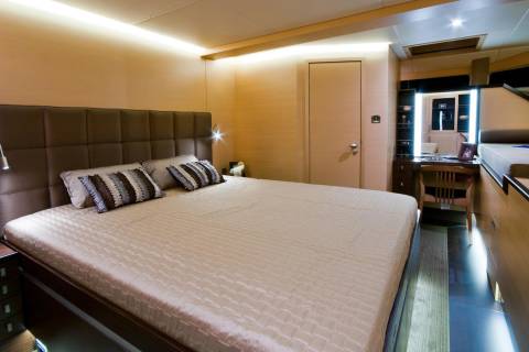 Luxurious bedroom aboard a yacht features a plush bed, elegant wood paneling, and ambient lighting.