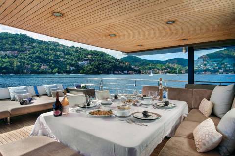 A beautifully set table awaits a delightful meal on a yacht, with a stunning coastal landscape as the backdrop.