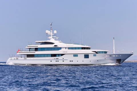 A sleek white superyacht named O'EVA cruises through the deep blue ocean under a clear sky.