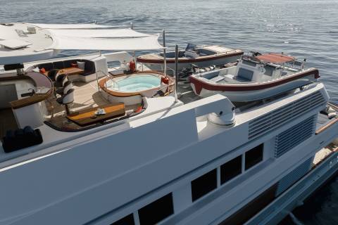 A luxurious yacht deck features a bubbling hot tub, plush seating, and two tenders ready for adventure on the sparkling blue sea.