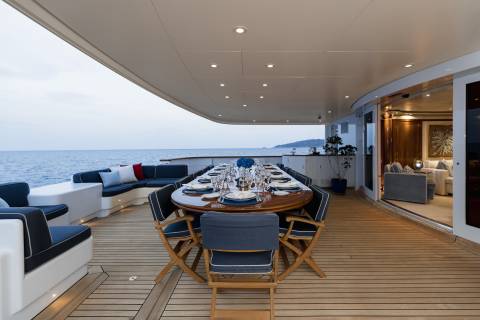 A beautifully set dining table awaits guests on the deck of a luxurious yacht overlooking the serene ocean.
