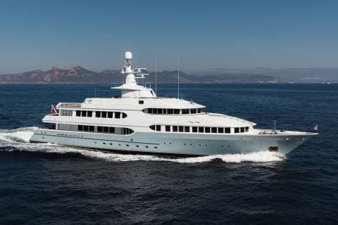A luxurious yacht cruises through the deep blue sea with a mountainous coastline in the background.