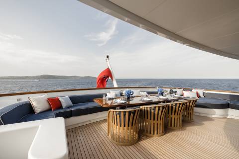 A beautifully set dining table awaits guests on the deck of a luxurious yacht, overlooking the serene blue sea.