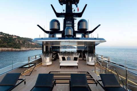Luxurious sun loungers and chic seating await on the expansive deck of this modern yacht, overlooking a serene coastal landscape.