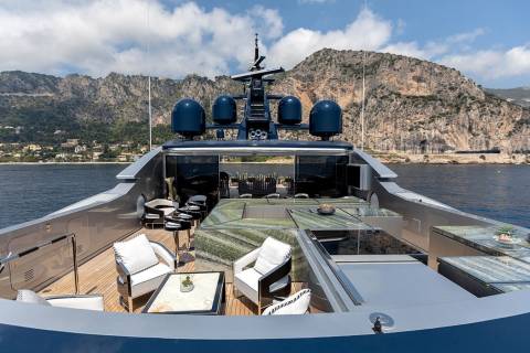 Luxurious yacht decks offer plush seating and dining areas against a backdrop of rugged coastal mountains.
