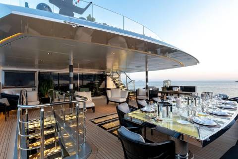 A lavish outdoor dining table is set for a feast on the deck of a luxurious yacht overlooking the serene ocean.