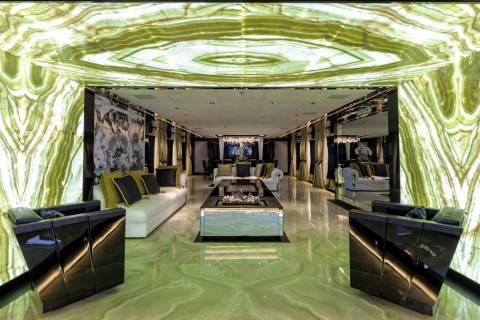 This opulent living space features luminous green onyx walls and floors, complemented by plush white sofas and a sleek glass coffee table.