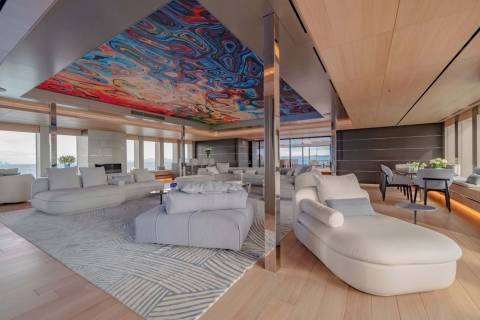 A luxurious yacht interior features a vibrant, abstract ceiling mural complementing plush white seating and expansive ocean views.