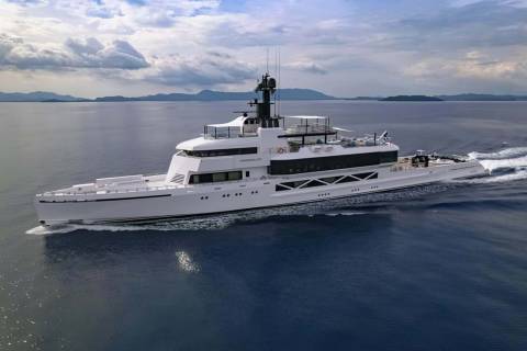 The luxurious yacht Wanderlust glides through calm blue waters with a mountainous coastline in the distance.