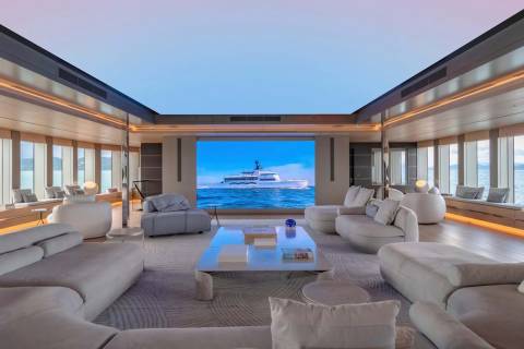 This luxurious yacht interior features a massive screen displaying a serene ocean view, complemented by plush seating and ambient lighting.