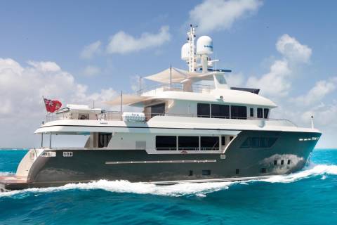 A large, luxurious yacht with multiple decks and a sleek, modern design is speeding across the vibrant turquoise waters of a tropical ocean, surrounded by fluffy white clouds in a bright blue sky.