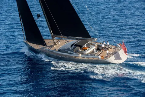 A sleek yacht with dark sails cuts through the deep blue ocean, its crew tending to the sails.